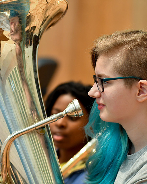 A female RCMJD student with tuba, sitting in rehearsal.